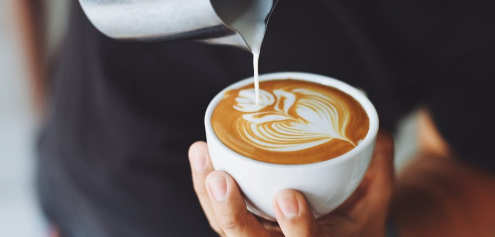 Man holding a coffee cup while making latte art